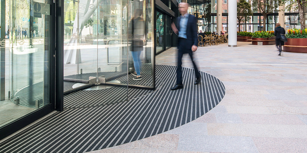 man exiting a building at a revolving door with barrier matting at doorway