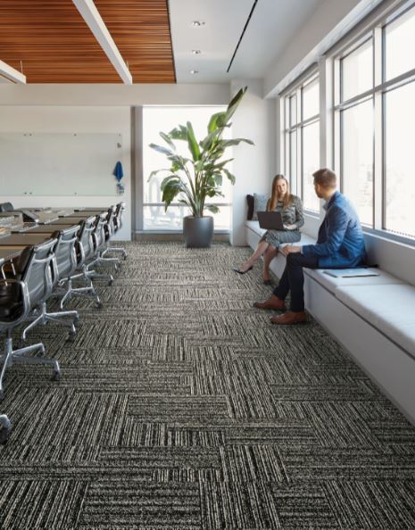 man and woman sitting on a bench in a office with black and white carpet tiles on the floor 