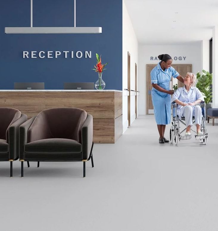 nurse pushing a old lady in wheelchair on top of grey commercial flooring at a reception desk